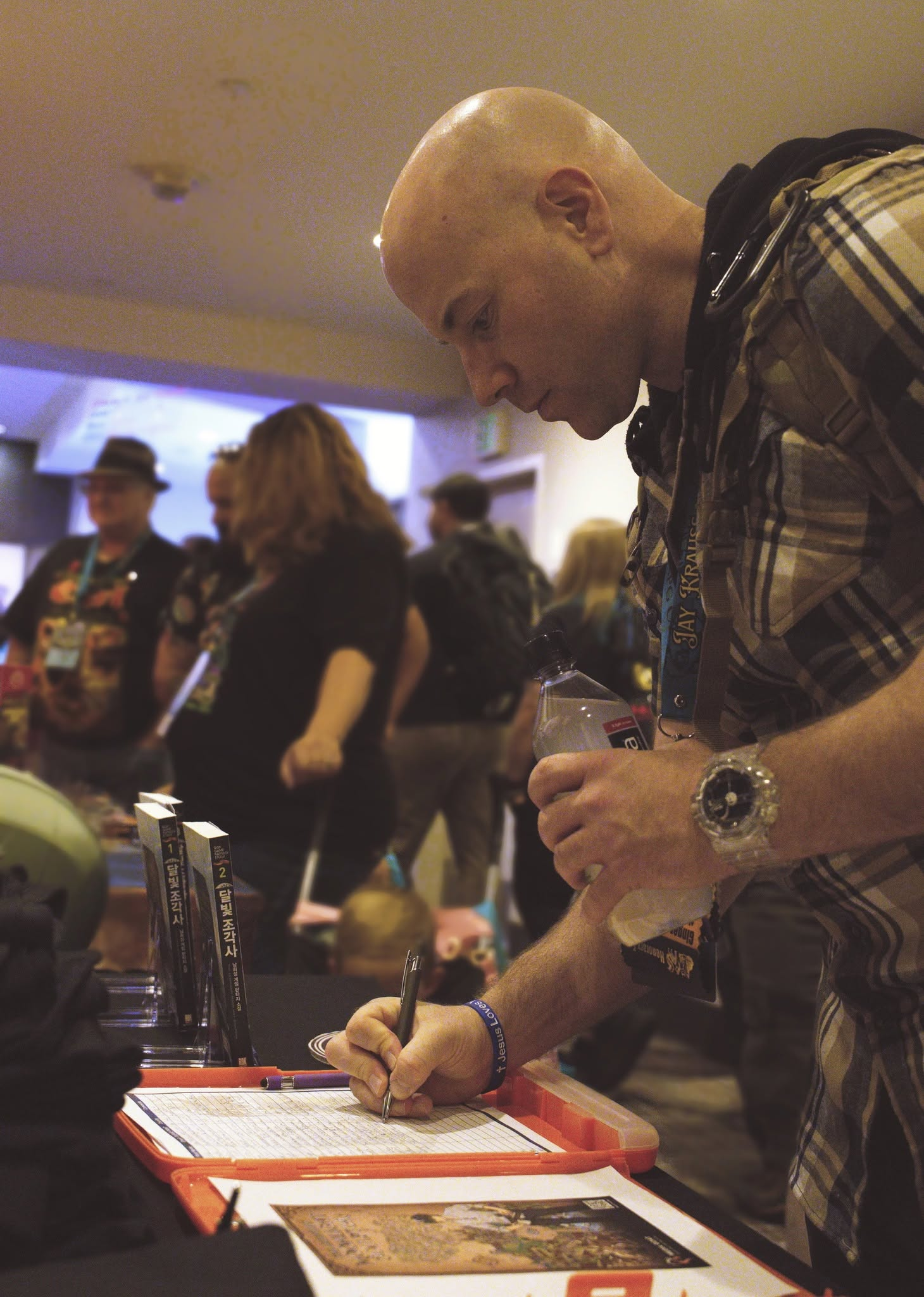 A man writing on a sign up sheet at a convention table.
